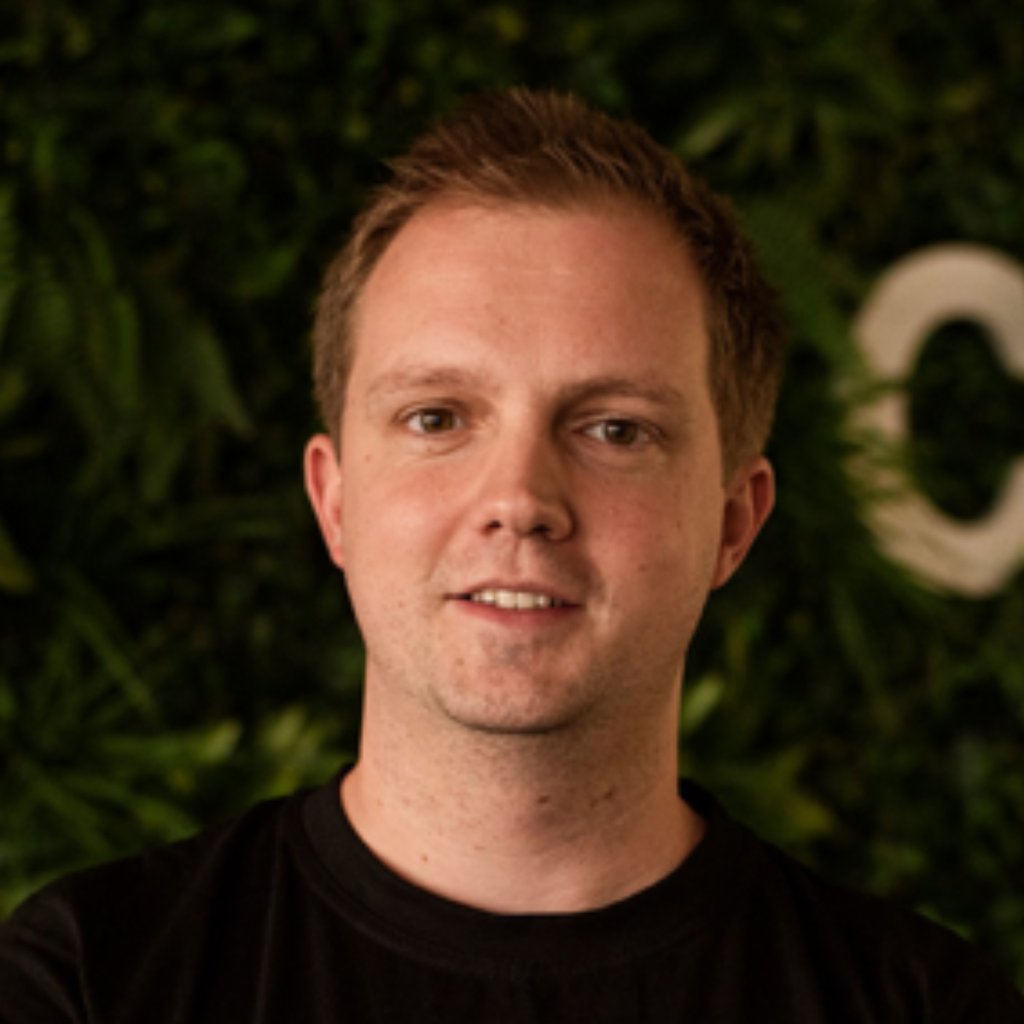 A man in a black T shirt in front of a grassy wall