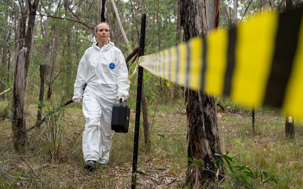 AFTER Director Maiken Ueland walking through the bush in a hazmat suit next to yellow and black warning tape.