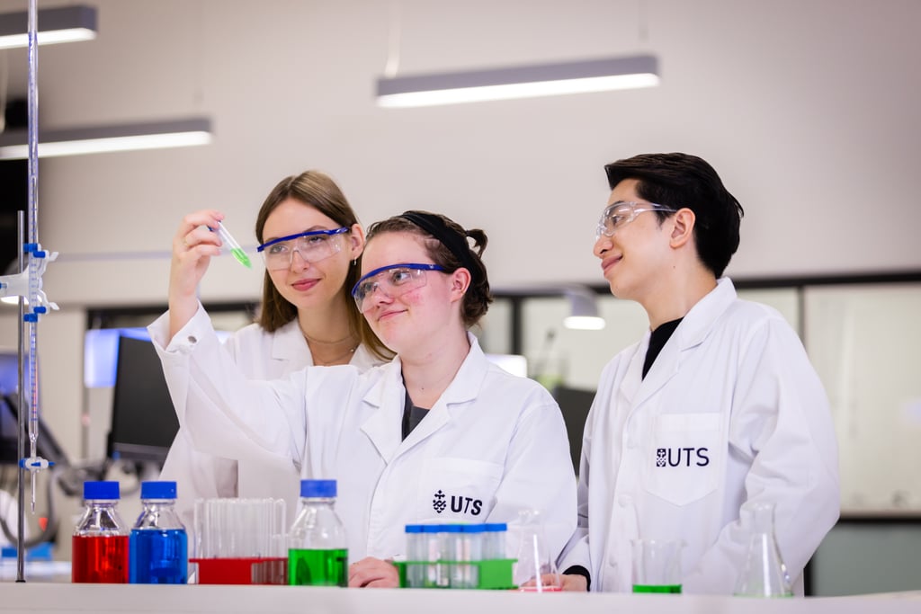 Three Science students wearing lab coats working together and observing a test tube.
