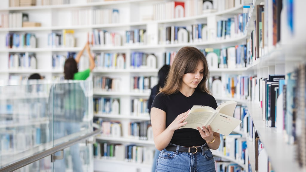Student standing in UTS Library looking through a book.