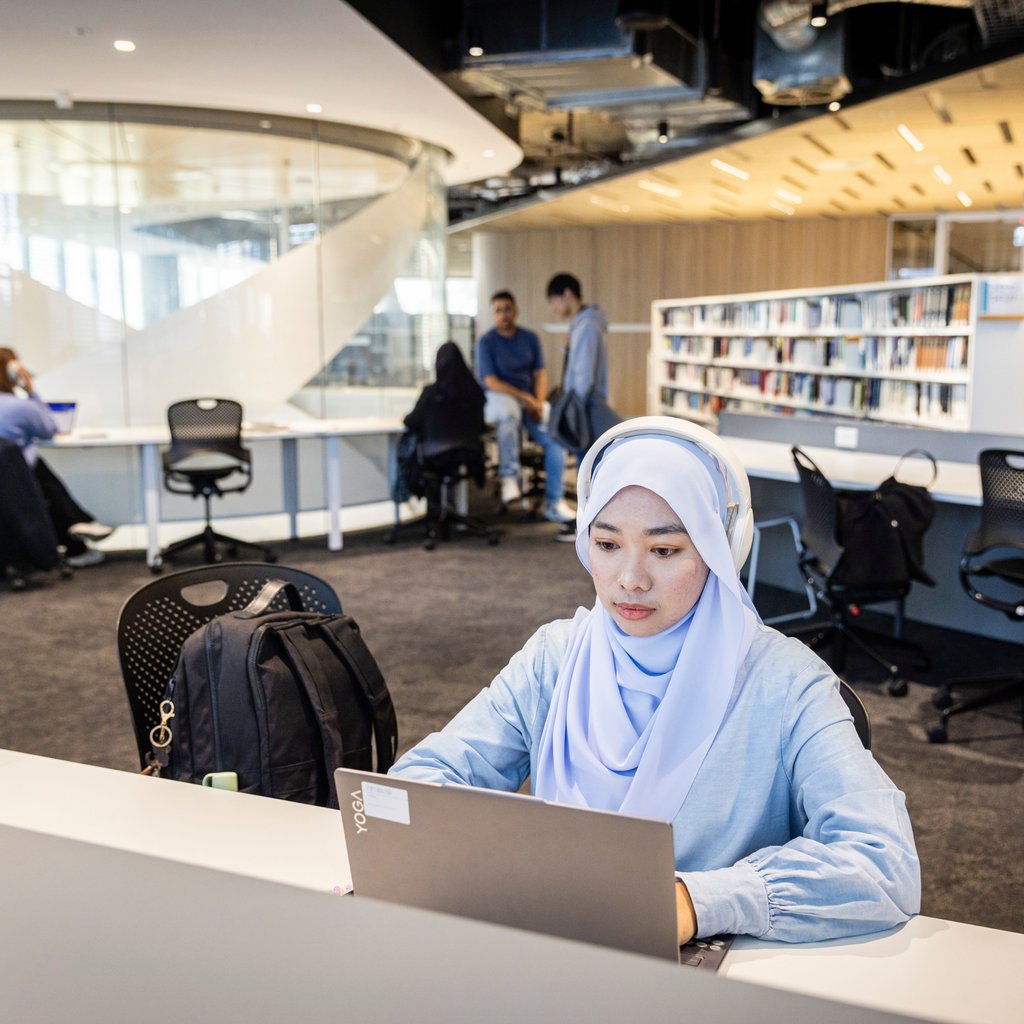 Female Malaysian student studies independently on laptop in UTS Library Building 2 Level 8. Keywords: study, exam, headphones, work.