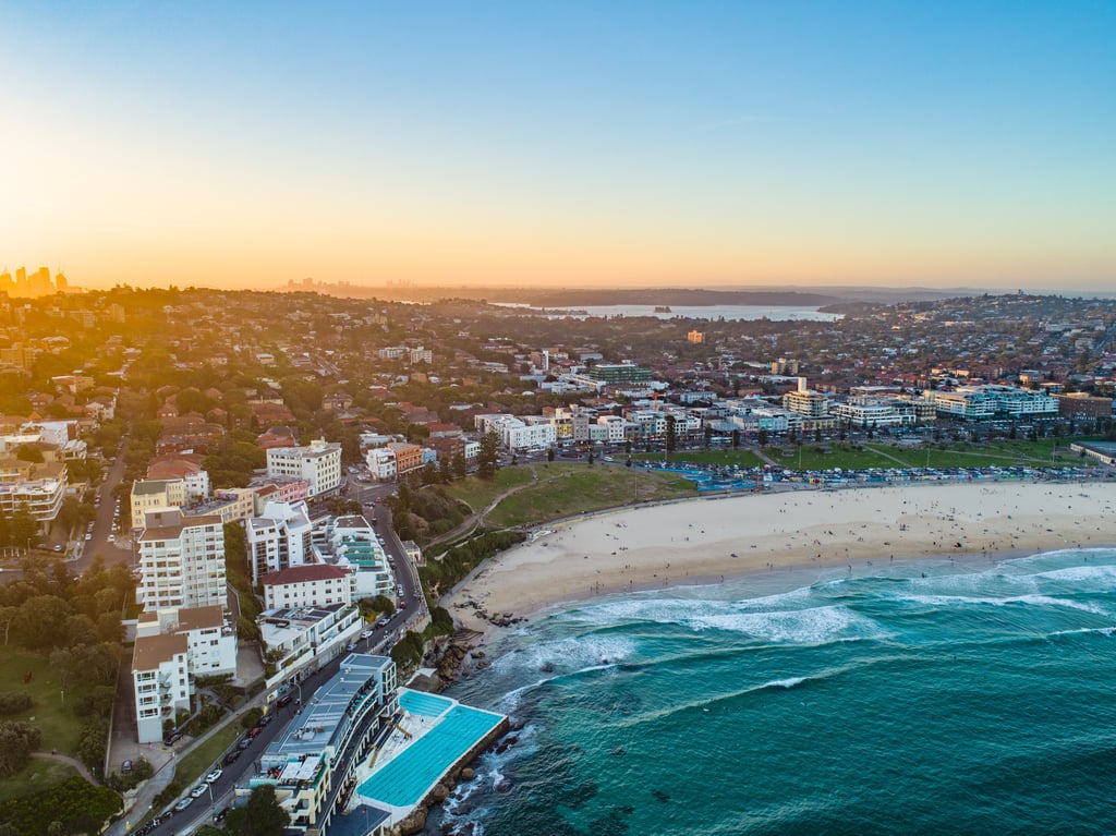 Panoramic Bondi Beach Drone Shot at Sunset with Sydney CBD in background.