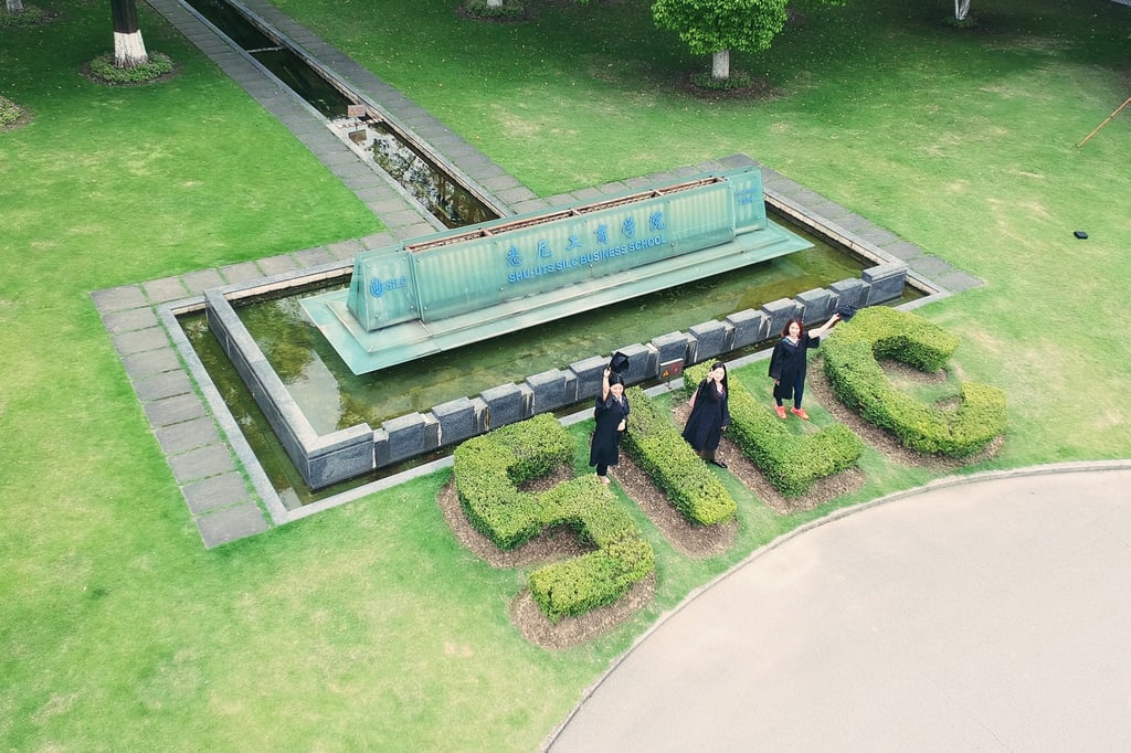 University graduates standing near a water feature and garden that says SILC Business School at Shanghai University.