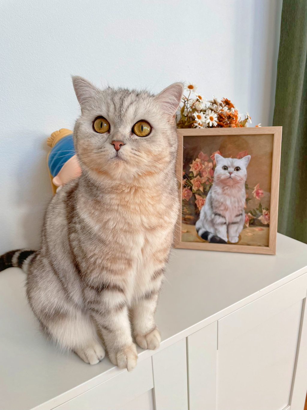 A cat sitting next to a portrait painted by Yuqing Wei.