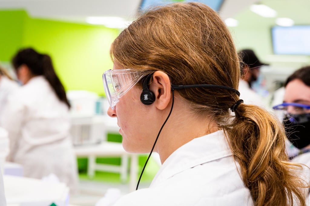 Student wearing the bone conduction headphone. Headphone is a small disc connected to a wire that wraps around the top ear.