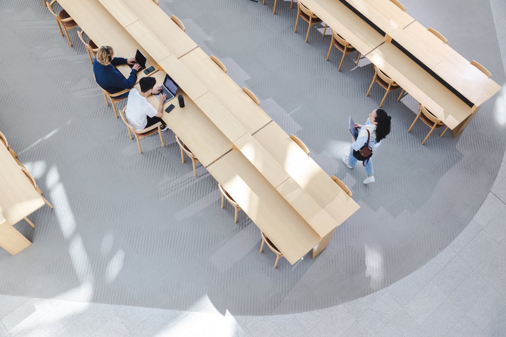 Aerial view of UTS Library Reading Room, with two students sitting studying at their laptops and another student walking past.