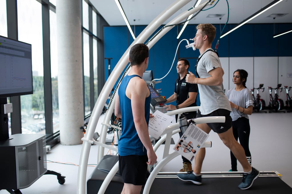 Athlete running on a treadmill being assessed by sports and exercise students.