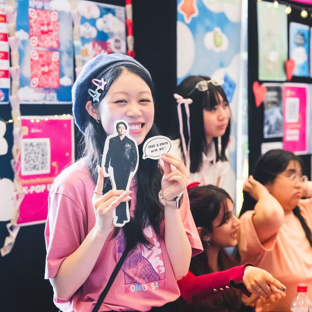 Student from K-pop society holding up small cutouts in front of stall.