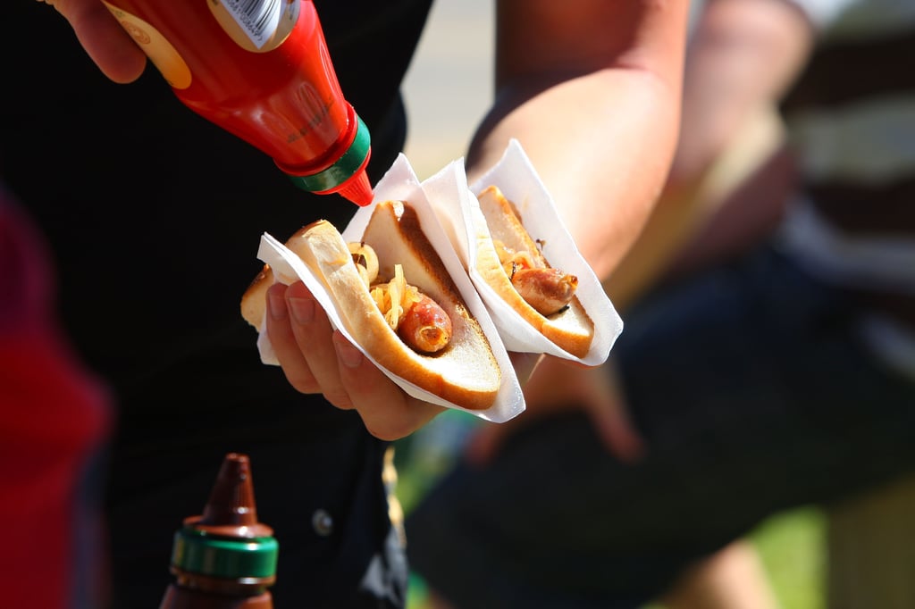 A hand holding two sausage sandwiches and putting tomato sauce on