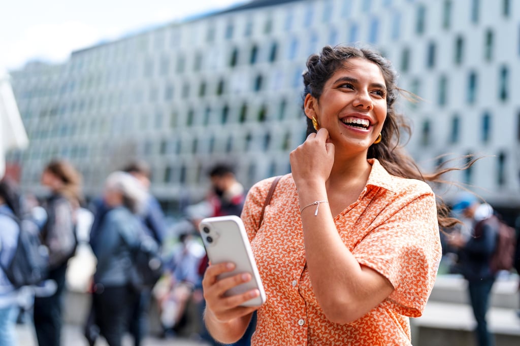 A woman smiles brightly while holding her cell phone, conveying joy and connection in front of UTS building.