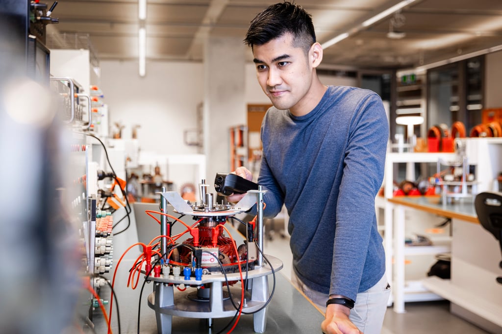 A focused man in a blue shirt works on a complex device with wires in a modern lab. The setting exudes innovation and concentration.