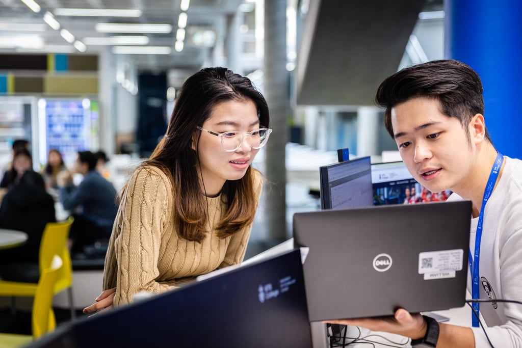Two international students engaged in discussion and reviewing content together on a desktop computer.