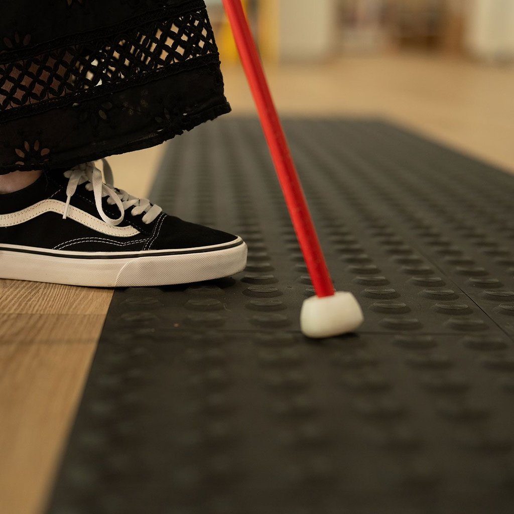 View of a person using a cane and tactile strips to navigate up stairs.