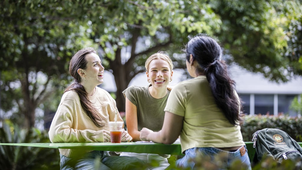 Three female students talk on green table