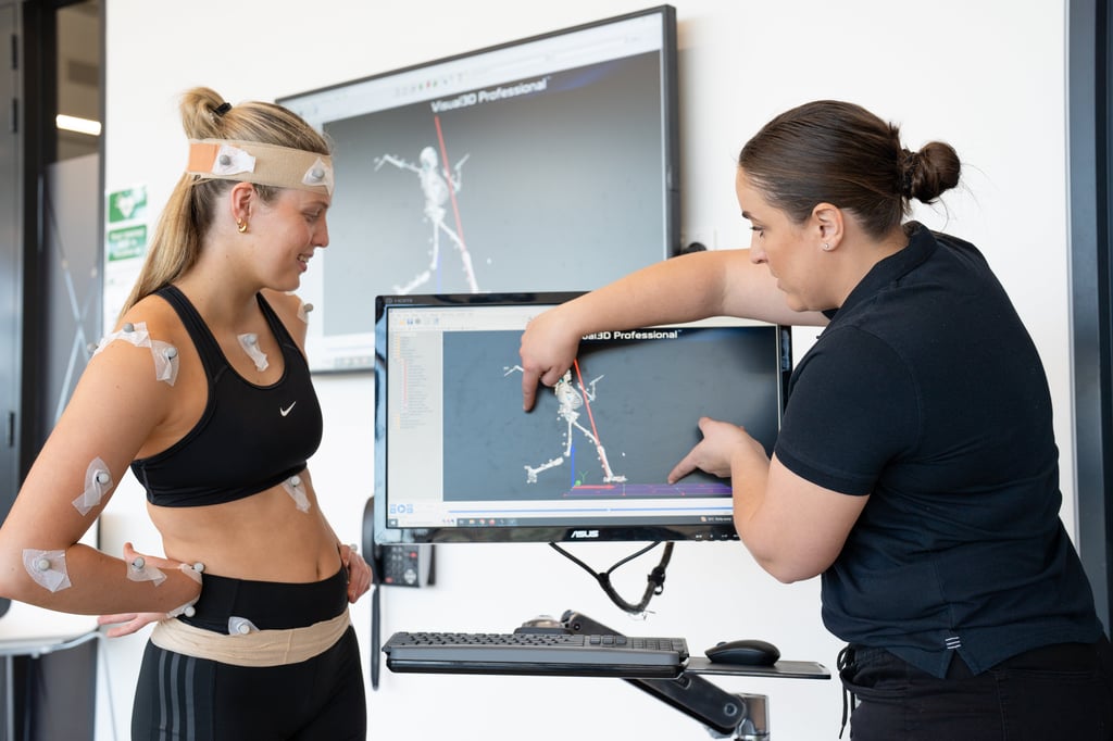 Dr Libby Pickering Rodriguez indicates renderings on a screen to an athlete covered in sensors
