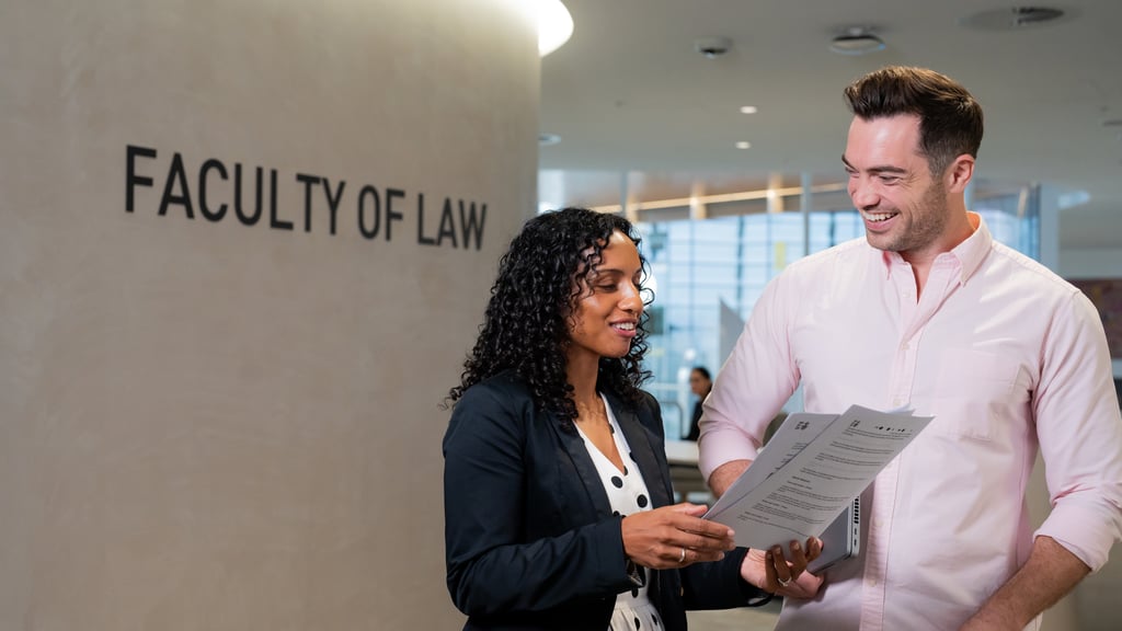 A woman and a man smile while discussing documents in front of a "Faculty of Law" sign.