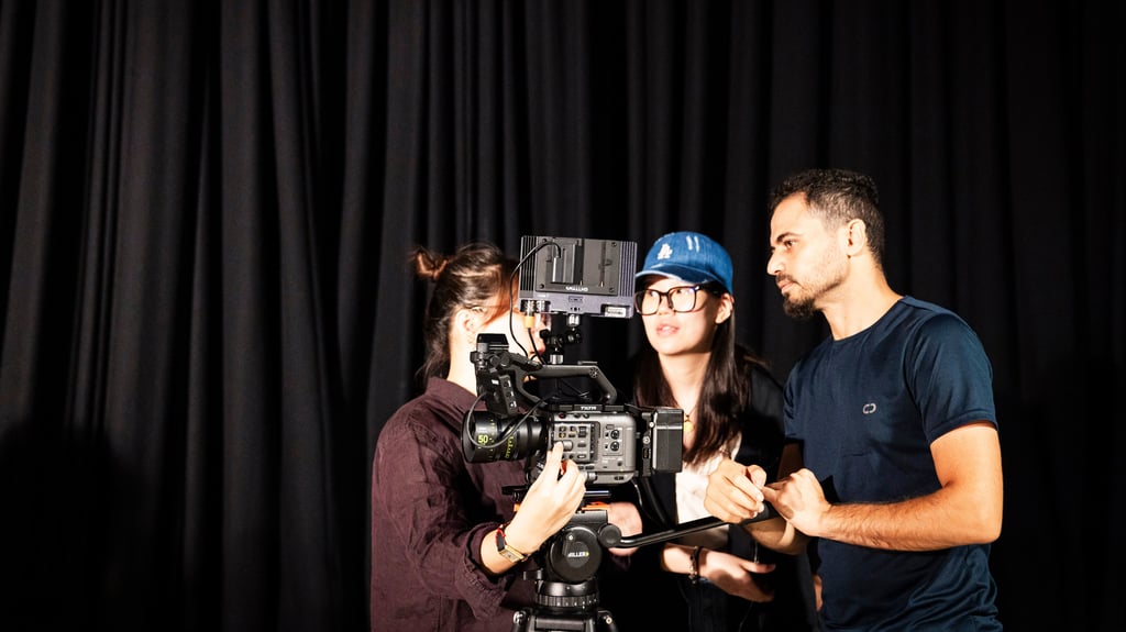 Three students standing around film camera in dark studio.