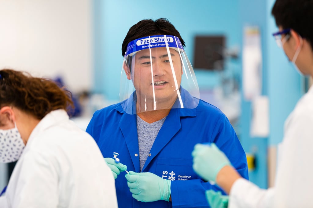 Student in the lab with a face shield, gloves and lab coat.