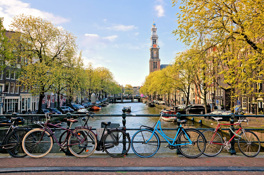 Bicycles lining a bridge over the canals of Amsterdam with church in background.