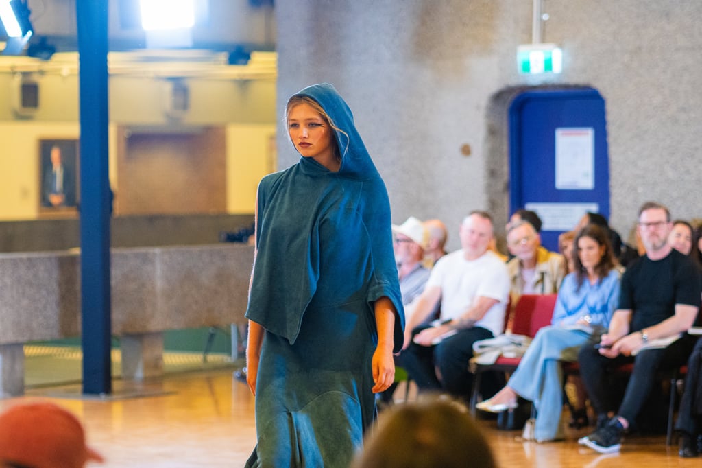A model wears a teal blue cloaked and hooded dress