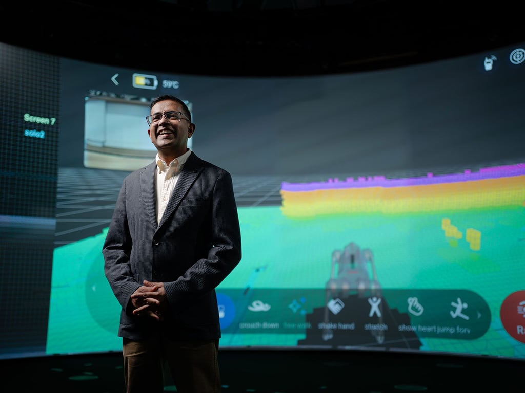 Professor Sarath Kodagoda, head of the UTS Robotics Institute, stands in the UTS Data Arena. A view of the robotic guide dashboard is visible on the screen behind him.