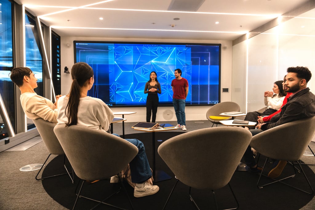 Male and female student presenting to five other students in the UTS Data Lounge with large screen behind them.