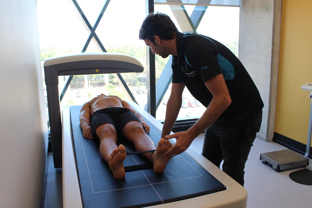 A person lies on a medical examination table while a technician adjusts their position.