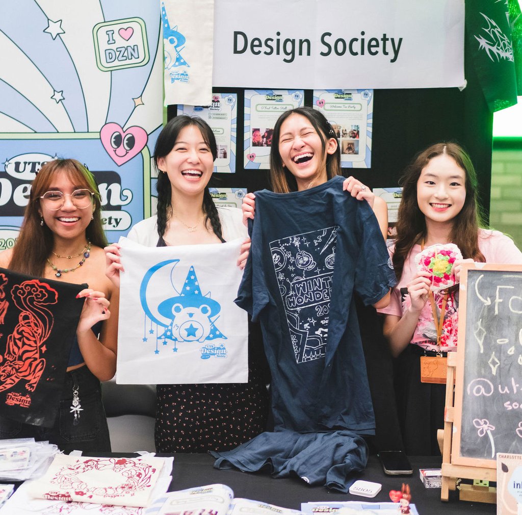 A group of students holding up prints in front of a booth sign the reads "design society"