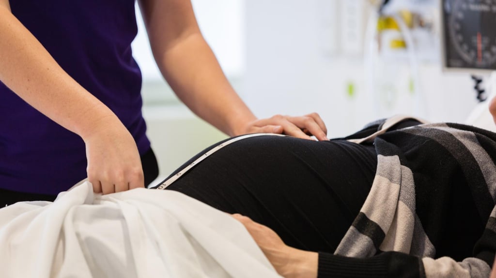A midwifery student measuring the stomach of a pregnant person in a hospital setting.
