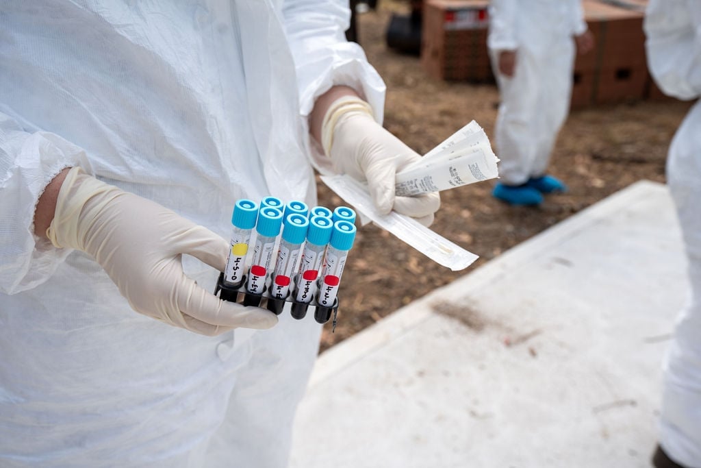 Close-up of a person in a hazmat suit holding test tubes.