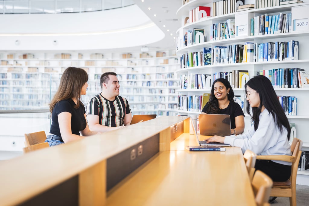 Group of students sitting at table in library.