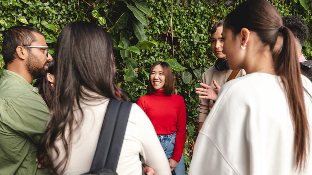 Male and female students standing chatting in a circle with green plant wall behind them.