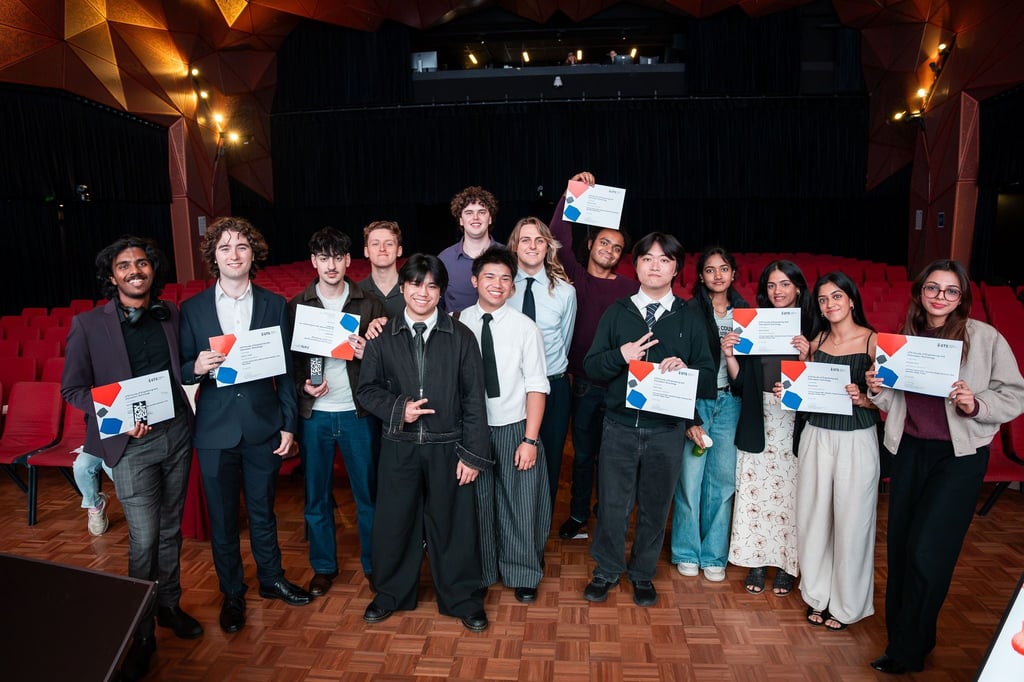 Tech Fest award recipients pictured smiling standing together with their awards. Recipients are standing in front of red chairs