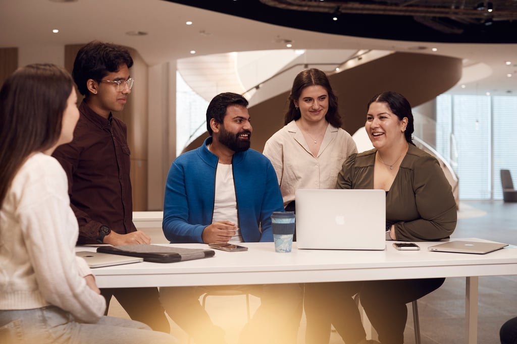 A diverse group of students gathered around a table, collaborating with a laptop inside a UTS building.