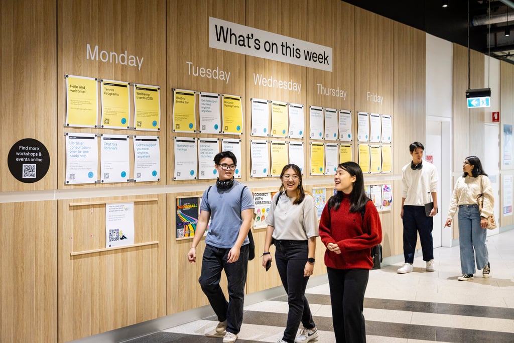 Three international students walking in Building 2 on the UTS Campus with a wall of posters behind them.