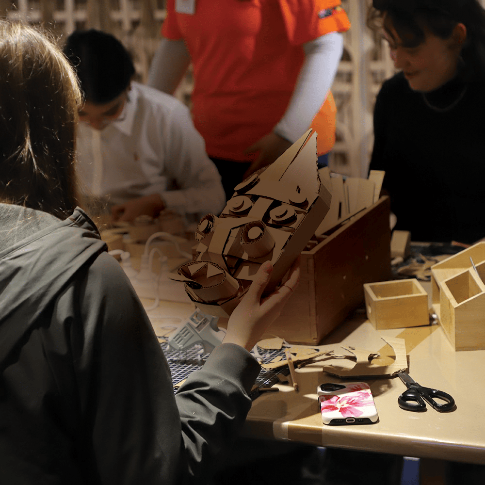Person holding a handmade cardboard face mask at a table during a craft activity.