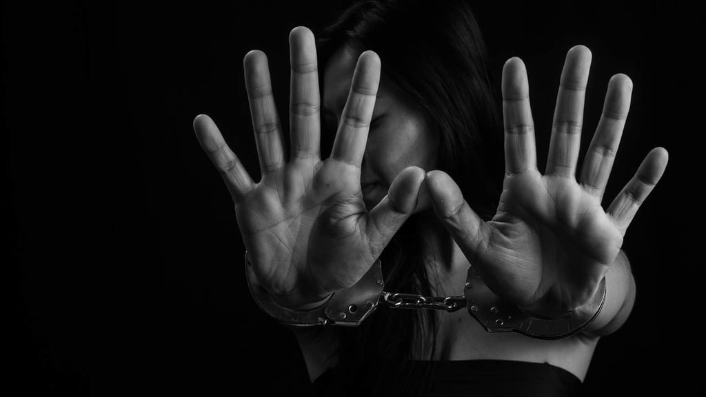 Black and white photo of a woman with long dark hair holding both handcuffed hands up toward the camera, palms facing out