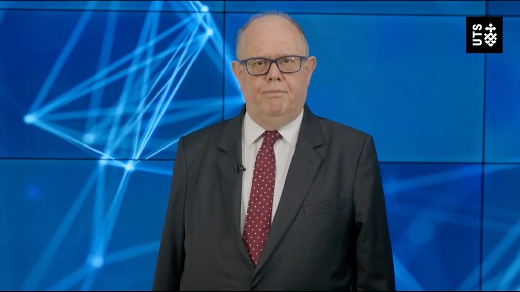 Andrew Parfitt, UTS Vice-Chancellor and President, standing in front of a large blue digital display featuring abstract network graphics.