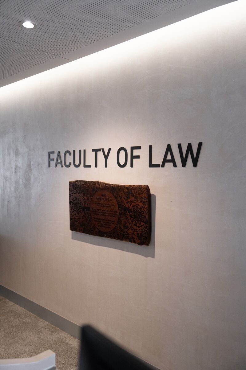 Entering the Faculty of Law, with "Faculty of Law" in black letters on a white wall above an Aboriginal artwork