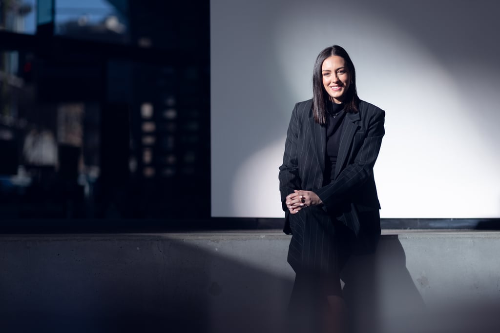 Georgia wears a black pinstripe suit and sits in front of a white wall