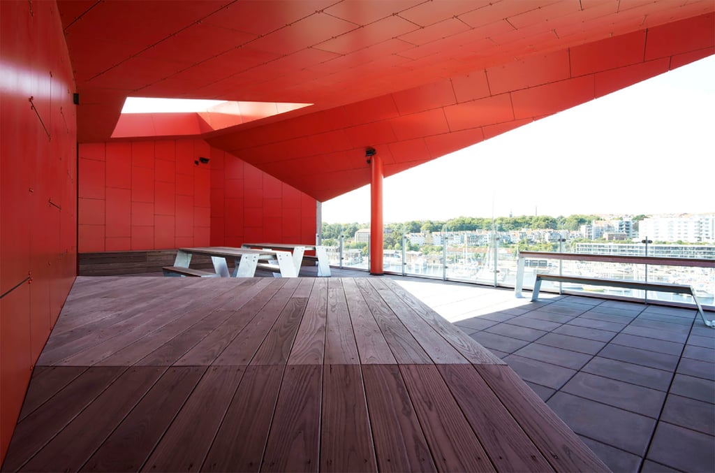 Looking out from a balcony in the Aarhus Student Housing that contains several tables with attached bench seating in the daytime.