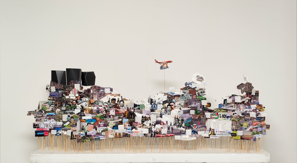 Art installation representing the city of Medellin consisting of pictures on paper and folded paper artefacts mounted on sticks of varying heights and embedded in a flat white base.