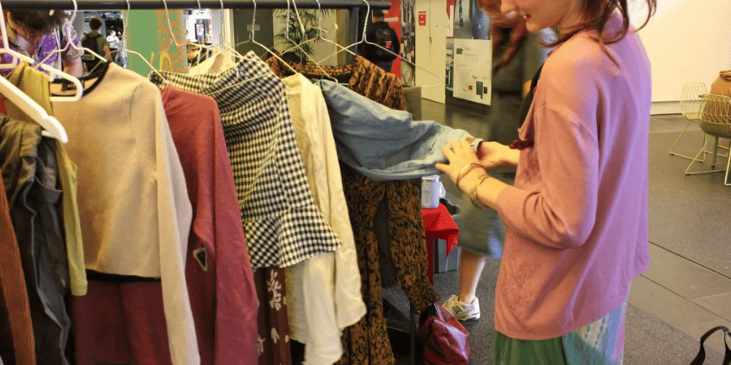 Person browsing a clothing rack filled with assorted second-hand garments.