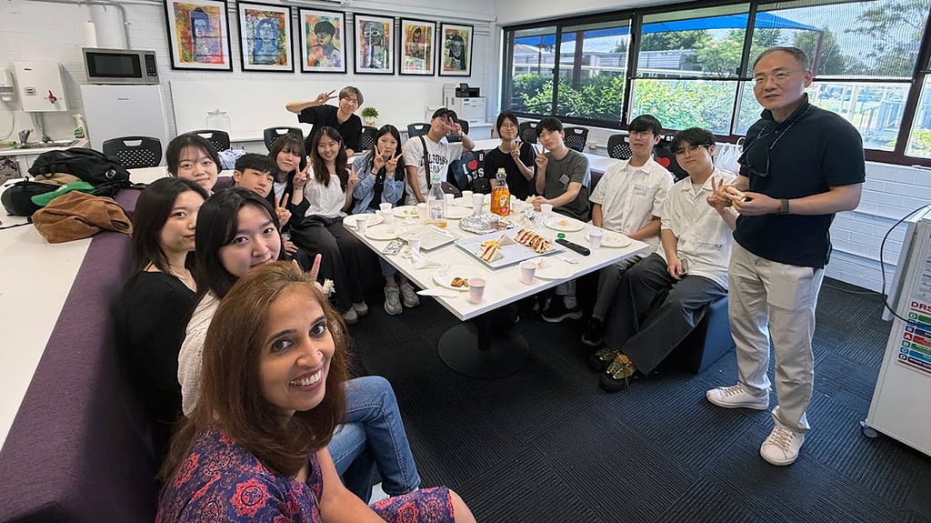 A group of students and others seated around a classroom table with a teacher standing alongside at Macquarie Fields High