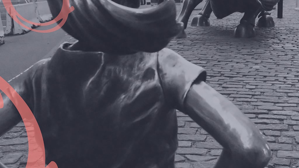Bronze statue of a girl stands defiantly, facing a large bull on cobblestone street.