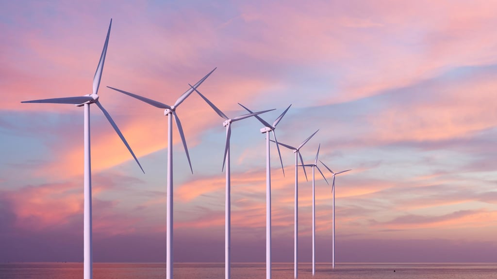 Row of wind turbines on calm sea at sunset, silhouetted against a vibrant sky in shades of pink and orange, conveying tranquility and sustainability.