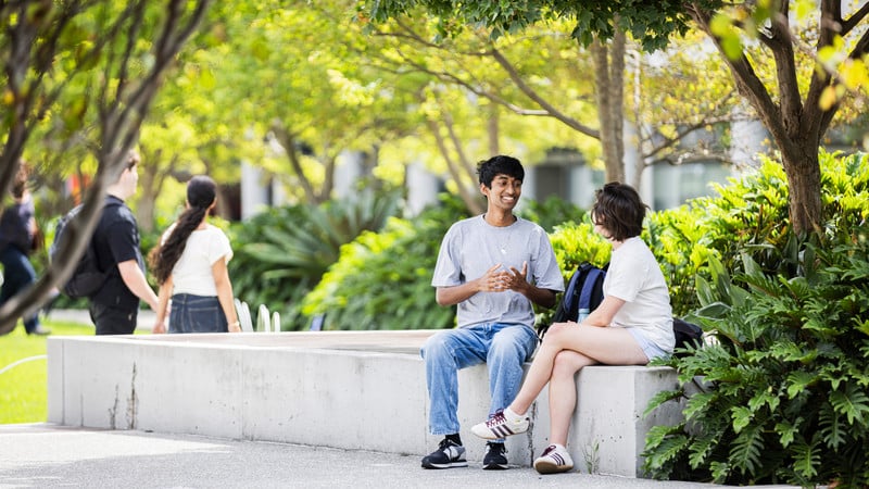 People sit in a landscaped outdoor UTS campus area with trees, gardens and concrete seating.