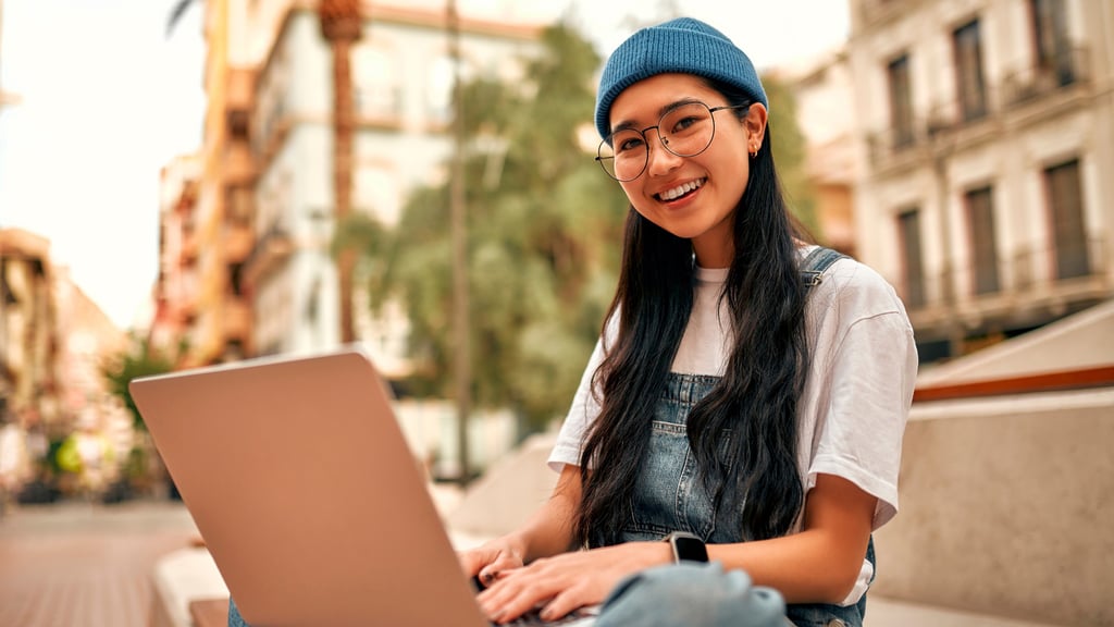 Smiling university student sitting outside with a laptop.