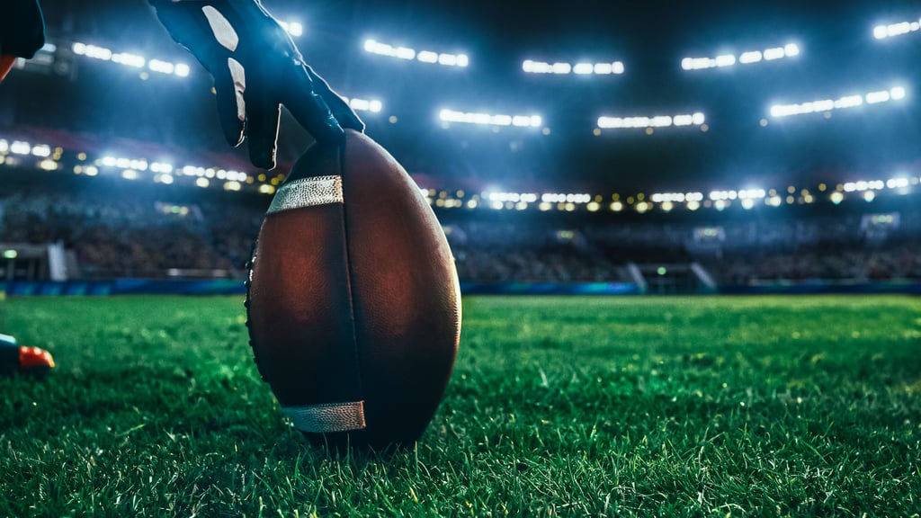 Close-up Shot of an American Ball Standing on a Stadium Field Held by Professional Player. Preparation for Championship Game. By Gorodenkoff/Adobe Stock