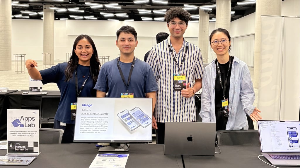 Four people smile at a tech booth displaying apps on screen. Signage reads "Apps Lab" at a startup summit. The atmosphere is professional and welcoming.